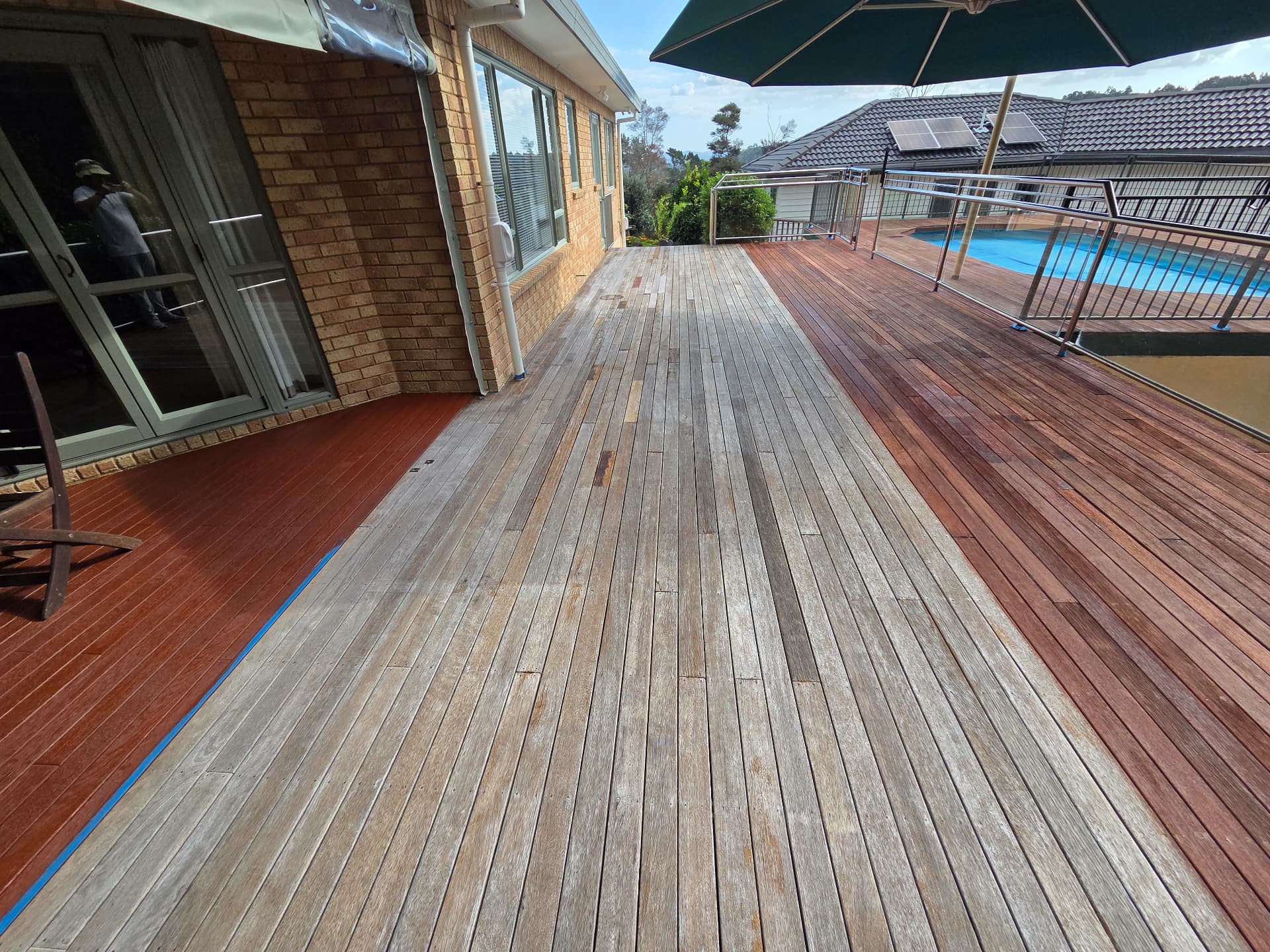 Poolside deck half stained rich red, half bare grey timber