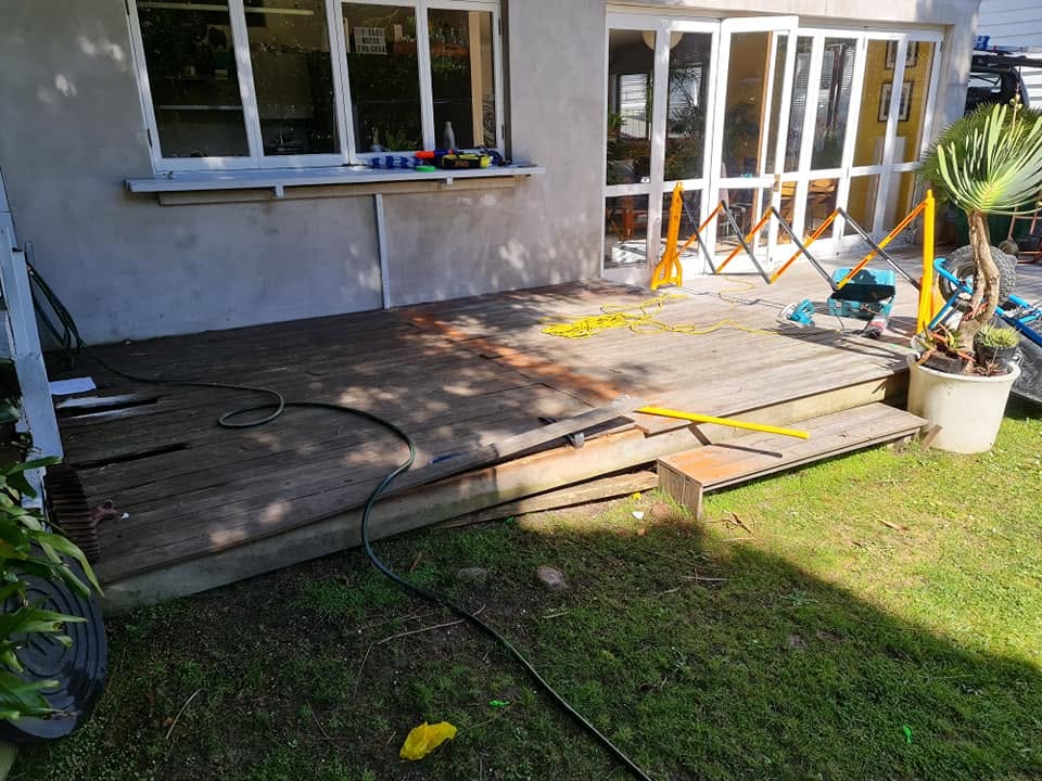 Rotten grey timber deck being pulled up beside a house